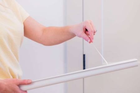 Close-up of peeling the adhesive backing off a white pull-side finger pinch protector door guard.
