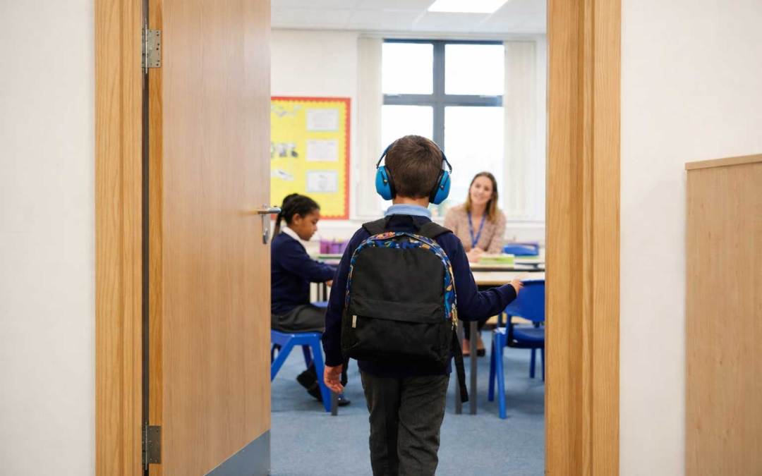 Elementary school classroom doorway with a child entering class, highlighting everyday door hinge risks for neurodivergent and autistic students.