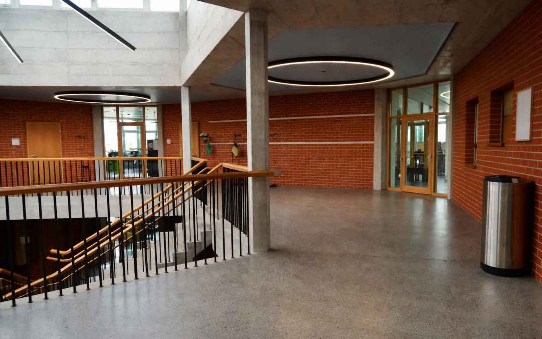 Modern educational building interior showcasing innovative materials, including exposed concrete, brick walls, glass doors, and contemporary lighting in a school atrium.